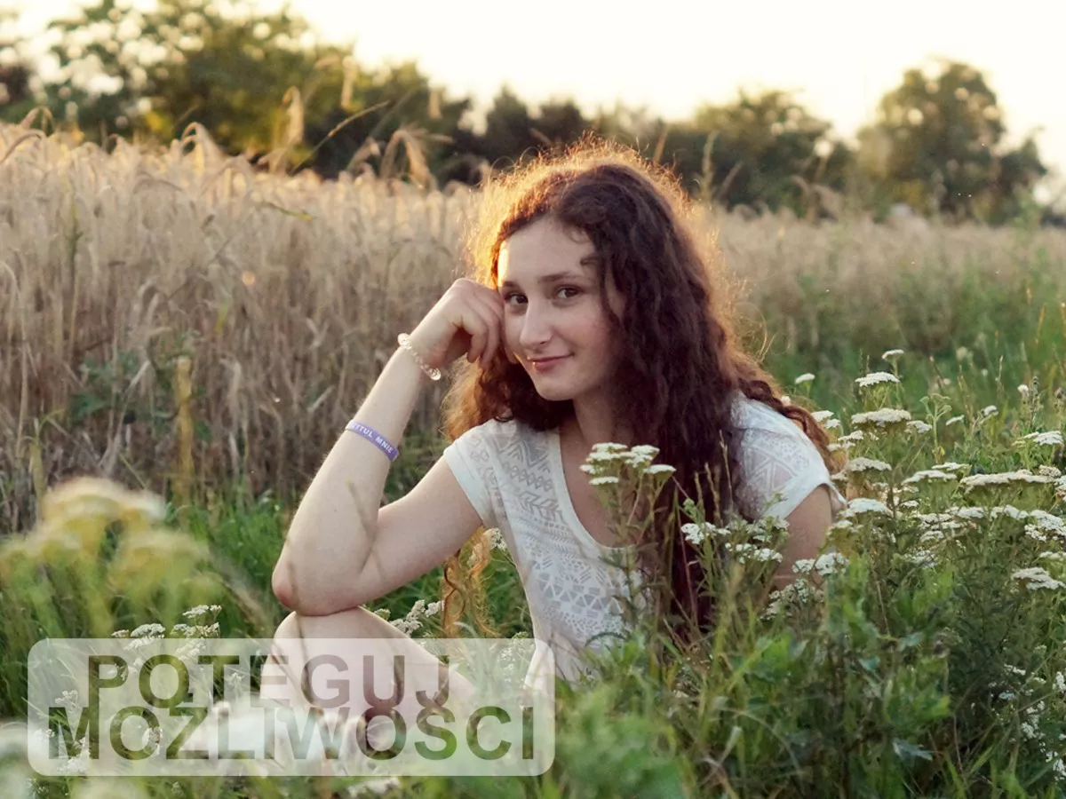 Studentka siedzi na łące na tle zboża.