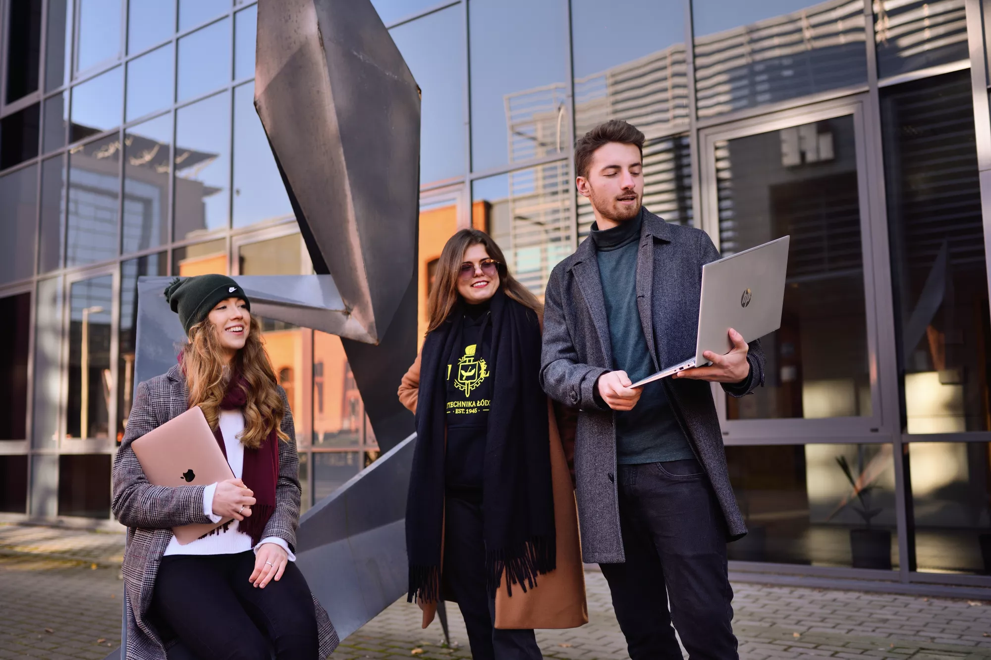 Studenci z laptopami stoją przed budynkiem.