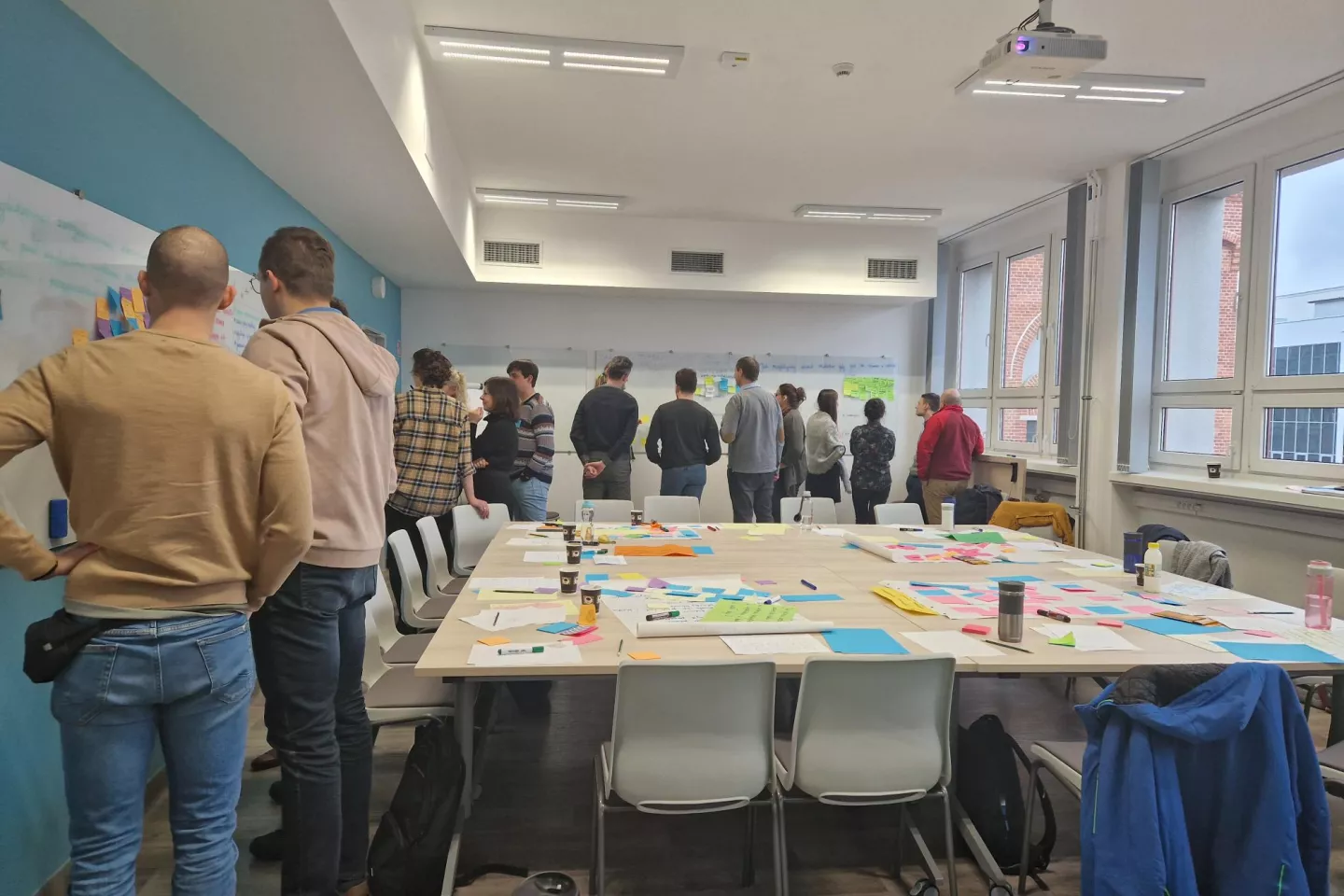 Grupa osób w sali pracująca przy tablicy nad projektem.