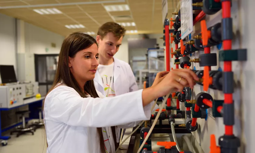 Studenci odkręcają kurek w instalacji w laboratorium.